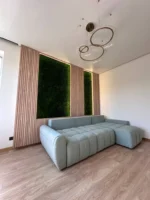 Paneele aus Flachmoos mit Beleuchtung und Leisten an den Wänden im Innenraum des Wohnzimmers mit hellem Sofa und Leisten